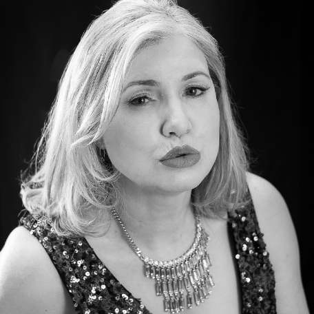 A blonde woman wearing a sequinned top and diamanté necklace pouts for the camera